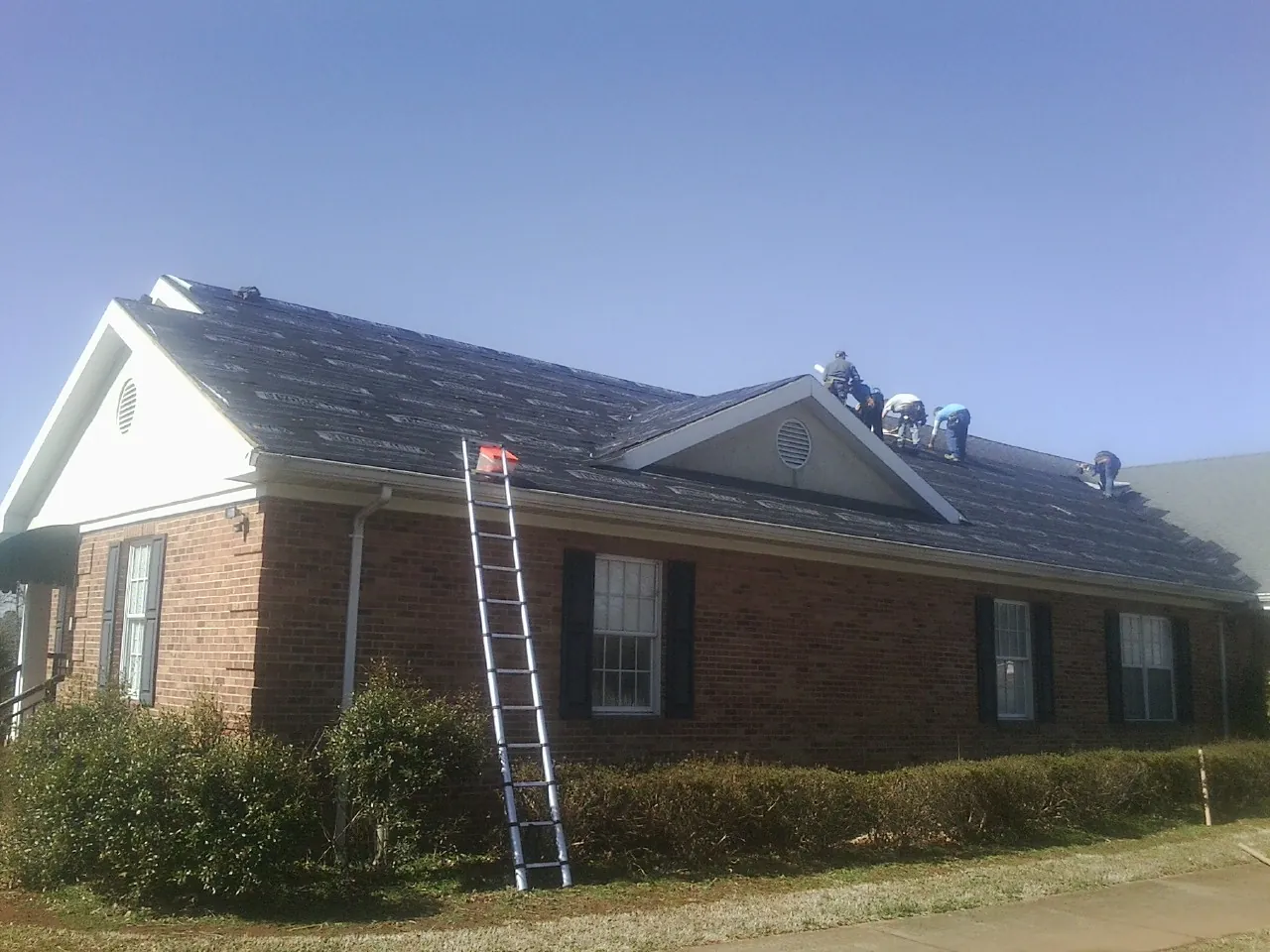 Crew tearing shingles off a brick ranch roof with a ladder set — Emergency Roof Repair work by our crew in Mifflintown