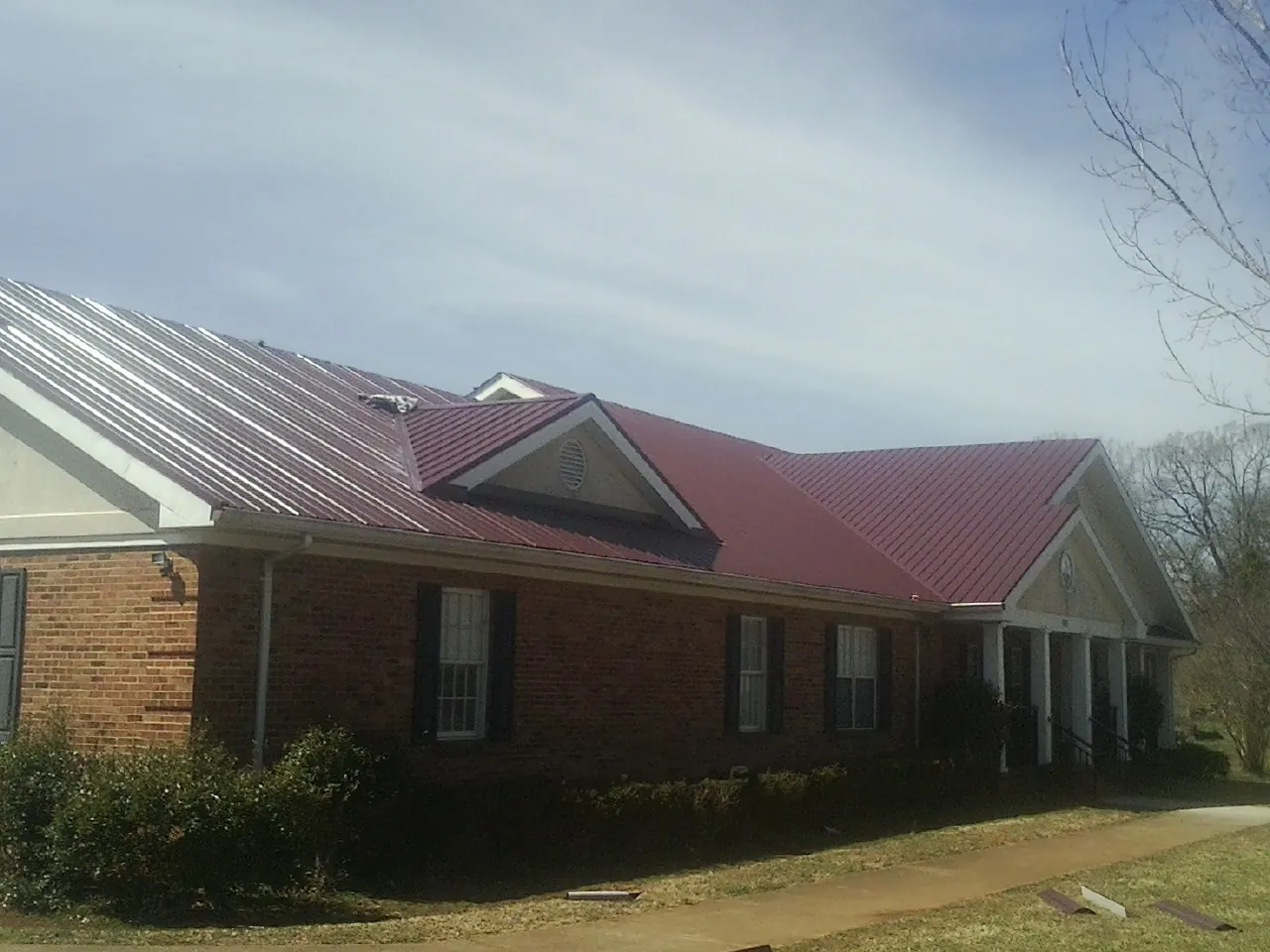 Red metal roof with gabled entries on a long brick building, from a Hail Damage Roof Repair job in Mifflintown