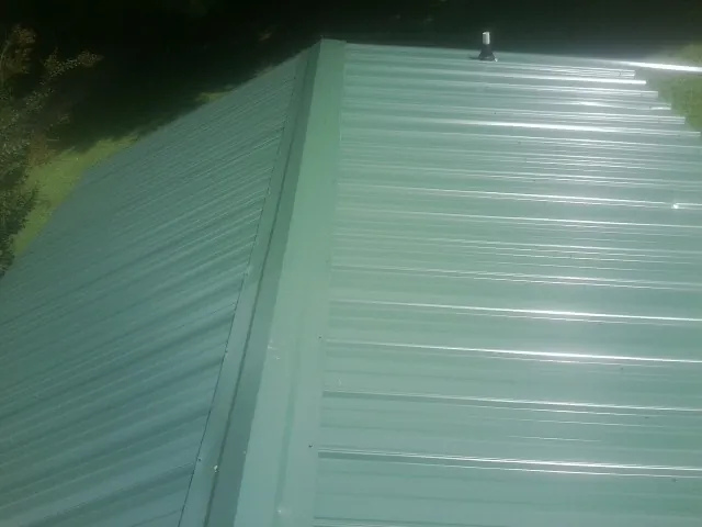 New green metal panels meeting at the ridge of a roof — Flat Roof Repair work by our crew in Mifflintown