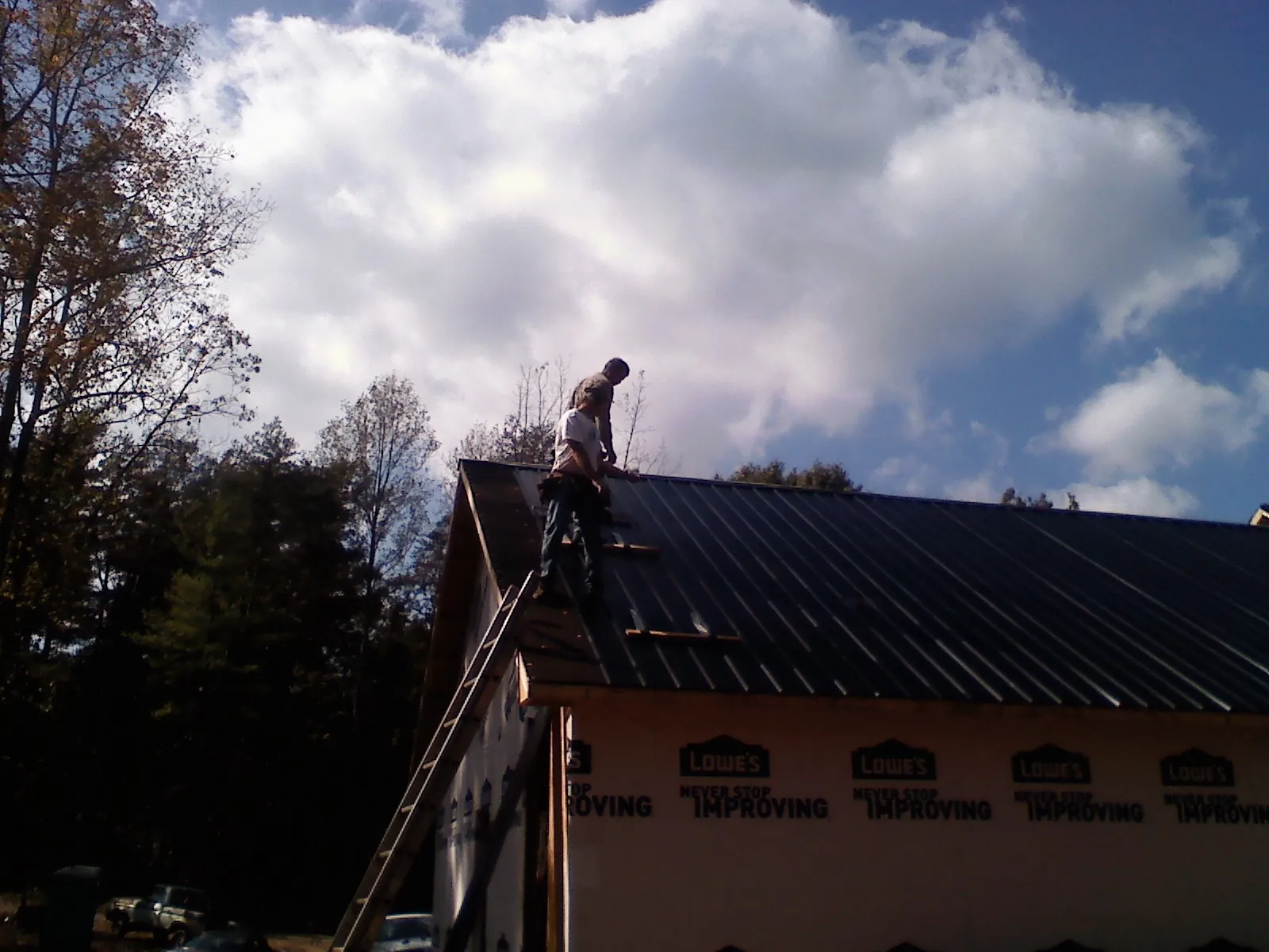 Roofer fastening dark metal panels high against a cloudy sky, from a Roof Inspection job in Mifflintown