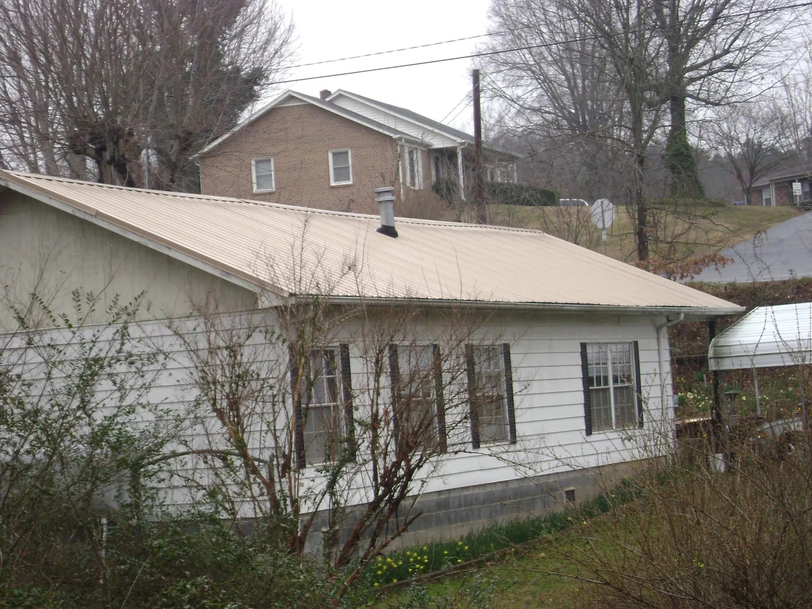 Tan metal roof on a white sided house set into a hillside — Commercial Roofing by Roofing Brothers in Mifflintown
